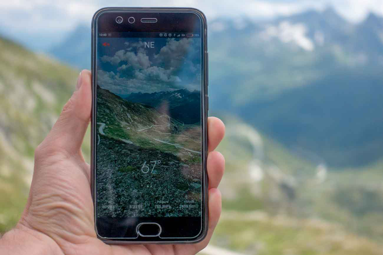 Ein Smartphone im Vordergrund, der Blick ins Tal im Hintergrund. Auf dem Smartphone ist eine Kompass-App geöffnet die anzeigt das ich mich auf 2459m Höhe befinde