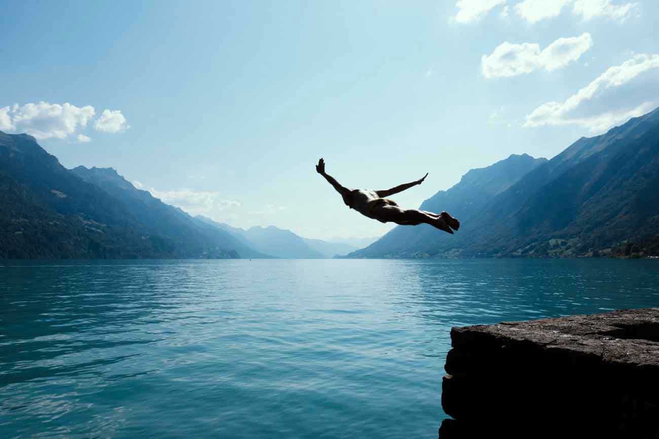 Patrick springt in den türkisfarbenen Brienzer See. Im Hintergrund ein Bergpanorama. Es sieht aus als wenn Patrick fliegt