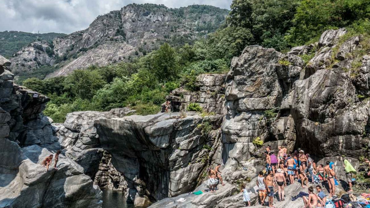 Viele Menschen stehen in Badebekleidung in den Klippen am Ufer des Flusses Maggia in der Schweiz