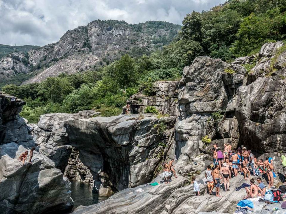 Viele Menschen stehen in Badebekleidung in den Klippen am Ufer des Flusses Maggia in der Schweiz