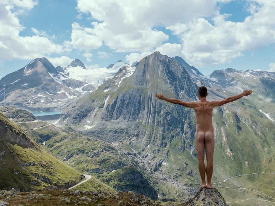 Patrick Arendt steht komplett nackt mit dem Rücken zur Kamera und guckt auf das Bergpanorama